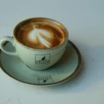A beautifully crafted latte art coffee in a Cafe Kangoo mug on a white marble table.